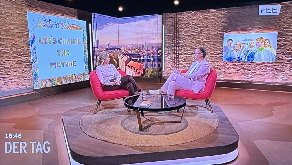 Screenshot der Sendung rbb-Sendung "Der Tag" am 15.05.25 Zu sehen ist Gesine Cukrowski, Schauspielerin, Autorin, Aktivistin, Feministin. Hinter ihr der Schriftzug "let's change the picture"